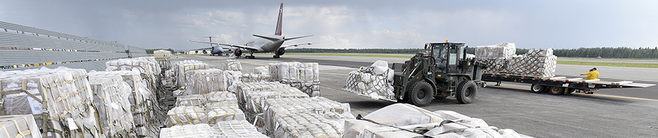 Wrapped pallets of cargo sitting in an airfield are loaded into a plane